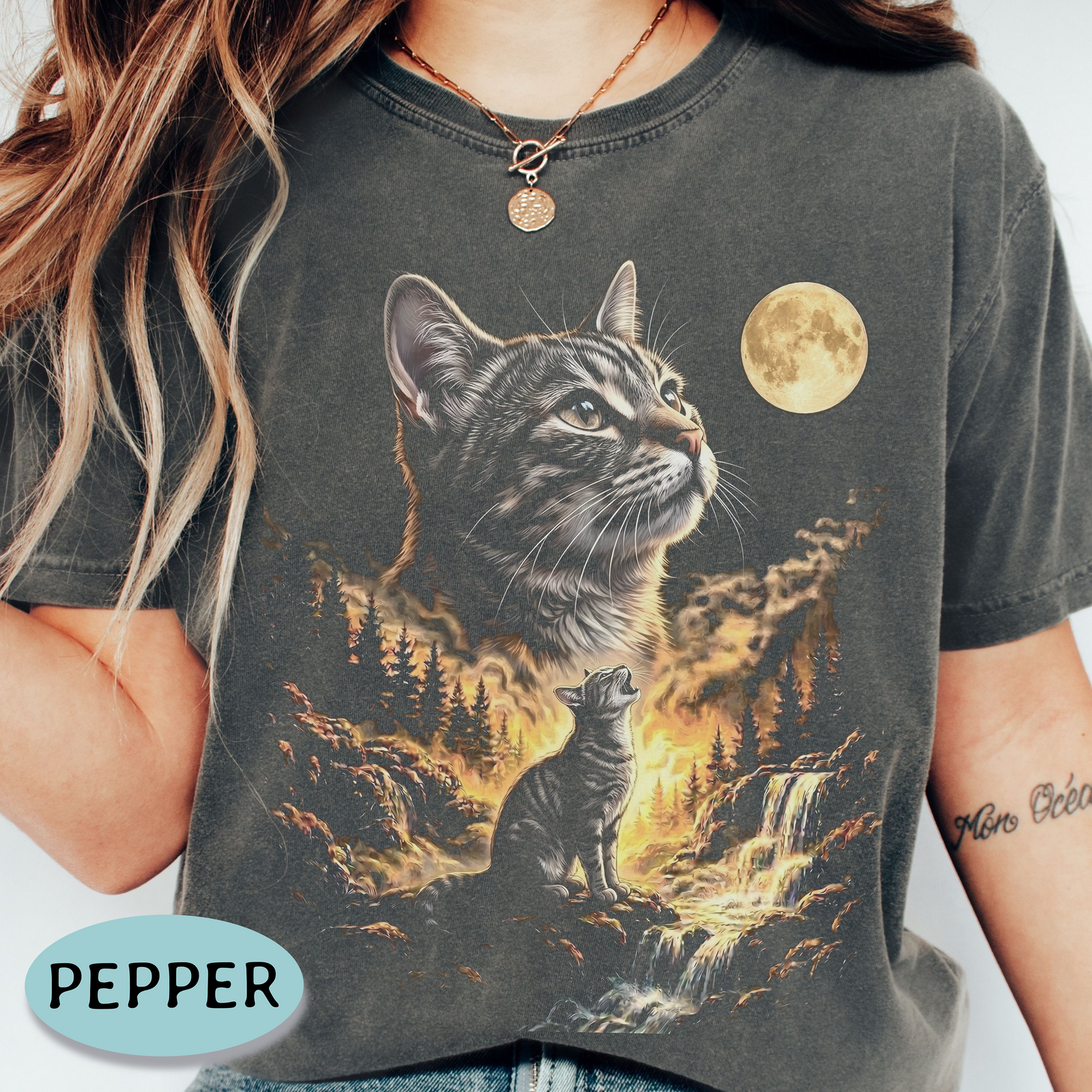 A person wearing a dark pepper gray graphic t-shirt featuring a detailed print of a tabby cat and a smaller cat in a forest landscape under a full moon.
