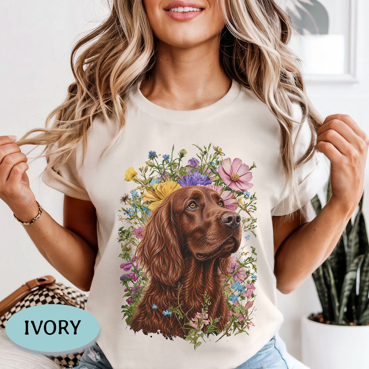 A woman wearing an ivory short-sleeve T-shirt with a large graphic print of a brown dog surrounded by colorful flowers. The image includes a light blue oval label in the bottom-left corner that reads 'IVORY'.