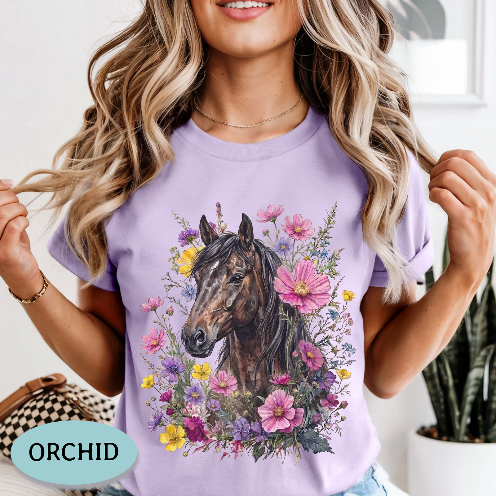 A woman wearing an ivory short-sleeve crewneck t-shirt with a graphic print of a brown horse surrounded by pink, purple, and yellow flowers. A light blue oval label in the bottom left corner reads 'IVORY'.